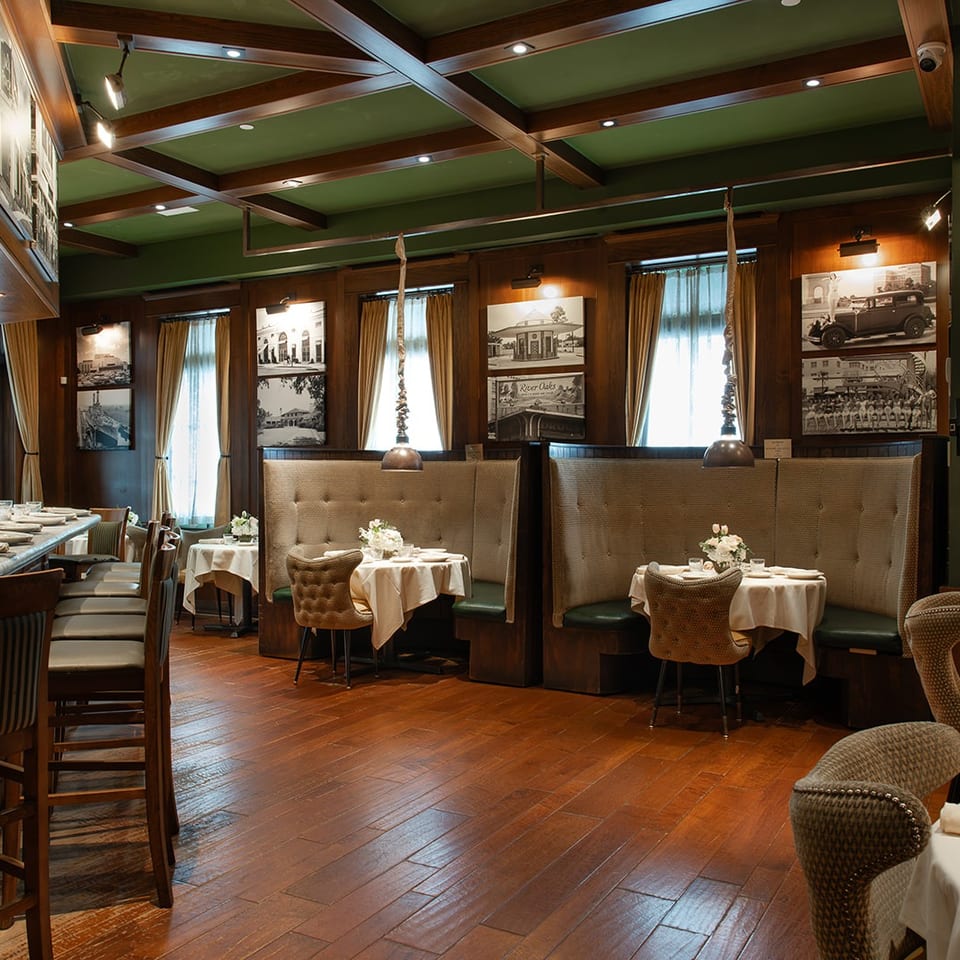 Elegant restaurant dining room with wood floors, green ceiling, leather booths, white tablecloths, and historic photographs.