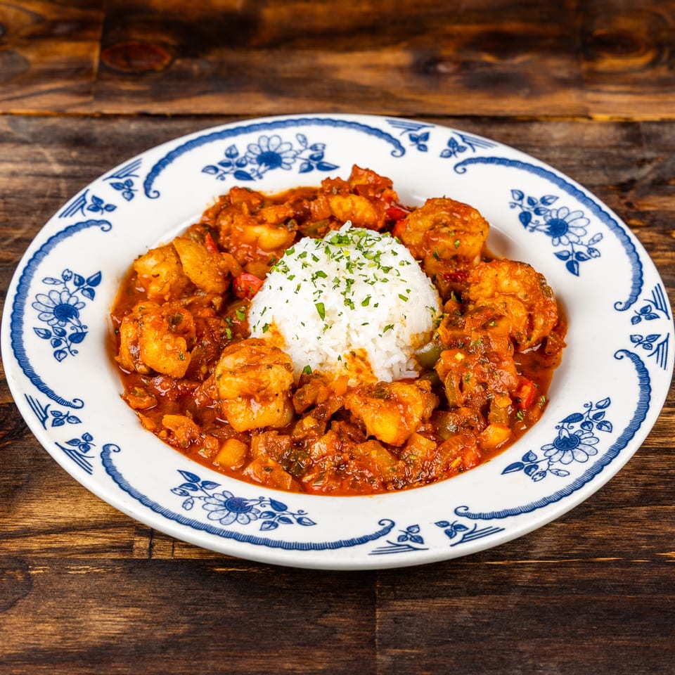 Spicy shrimp in tomato-based sauce surrounds a mound of herb-garnished white rice on a blue-and-white plate.